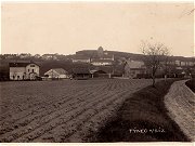 Pohlednice z roku 1932 zachycuje Tnec se severn strany. Na pohlednici je ada zajmavch objekt, jako je star hrad s v, budova tneck manufaktury na kameninu a star kola. Krom toho vak pohlednice zachycuje tm cel tneck ndra. V lev sti snmku zaujme rozen vpravn budova, kter proti pvodnmu stavu zskala nov patro. Uprosted snmku je vidt devn skladit s kamennou bon rampou. V prav sti pohlednice zaujme nkolik odstavench krytch nkladnch voz. 